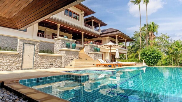 A modern two-story house with a swimming pool, stone walls, and a balcony overlooking the pool.