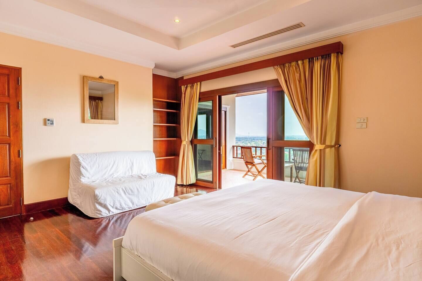 Habitación de hotel con una cama grande, una cama más pequeña, un balcón con una silla y vistas a la ciudad.