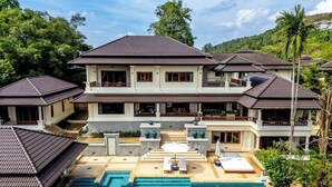 A large, multi-story house with a swimming pool, multiple balconies, and a well-maintained garden.