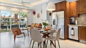 Eine moderne Küche mit Holzschränken, einem Edelstahlkühlschrank und einem Essbereich mit Glastisch und Stühlen.