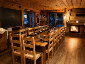 A long wooden dining table with chairs, a fireplace, and windows.