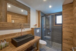 A modern bathroom with a wooden vanity, a large mirror, a black sink, a white toilet, and a glass shower enclosure.
