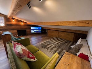 Una sala de estar acogedora con techo de madera, televisor de pantalla plana, sofás verdes y un tapete estampado.