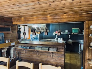 A rustic kitchen with wooden walls, a central island, hanging copper pendant lights, and a visible sink area.