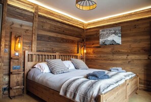 A wooden room with a bed, wall-mounted lights, and a framed picture.