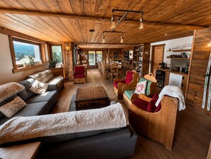 A cozy cabin interior with a sofa, chairs, wooden shelves, and a dining area.