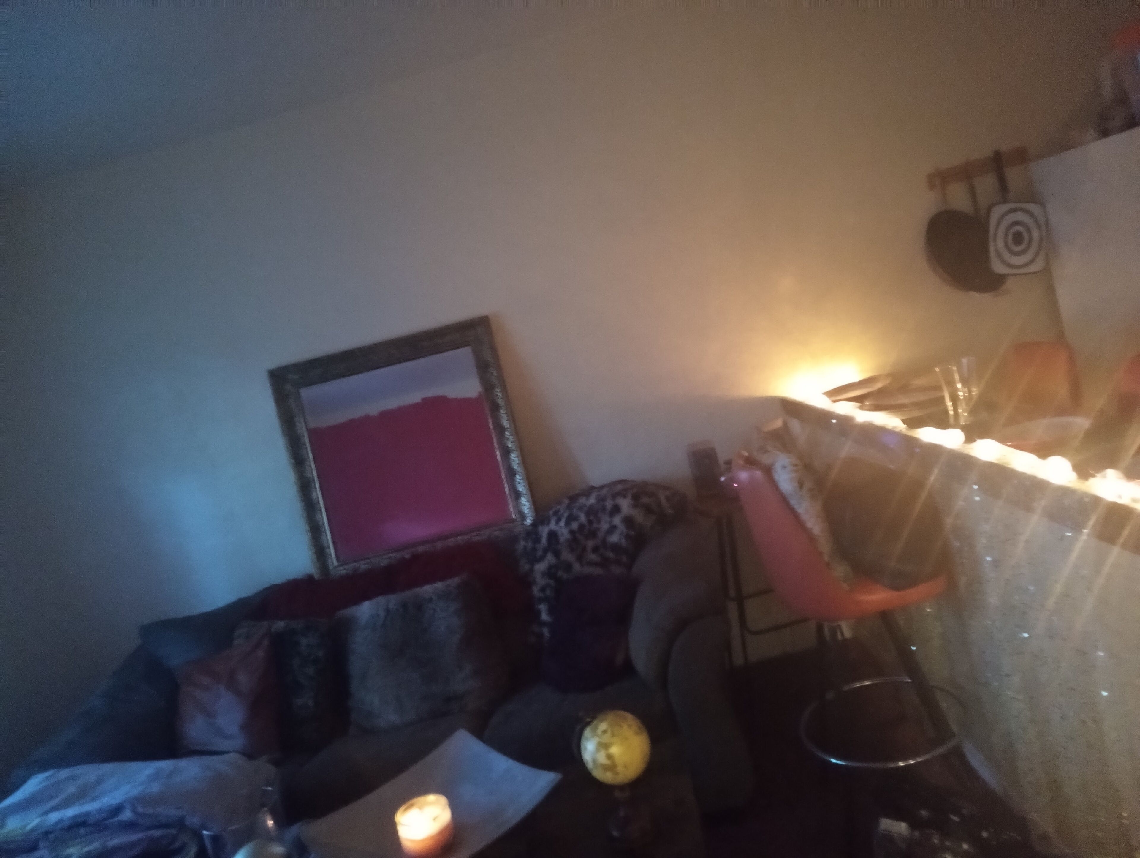Una habitación tenuemente iluminada con un sofá, un cuadro enmarcado en la pared, una mesita con una vela y un vaso de agua.