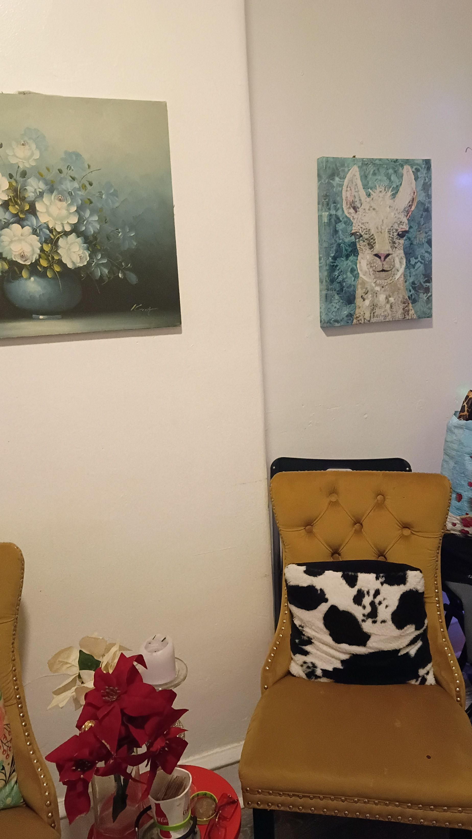 A room with a chair, a table with a red flower, and two wall-mounted artworks.