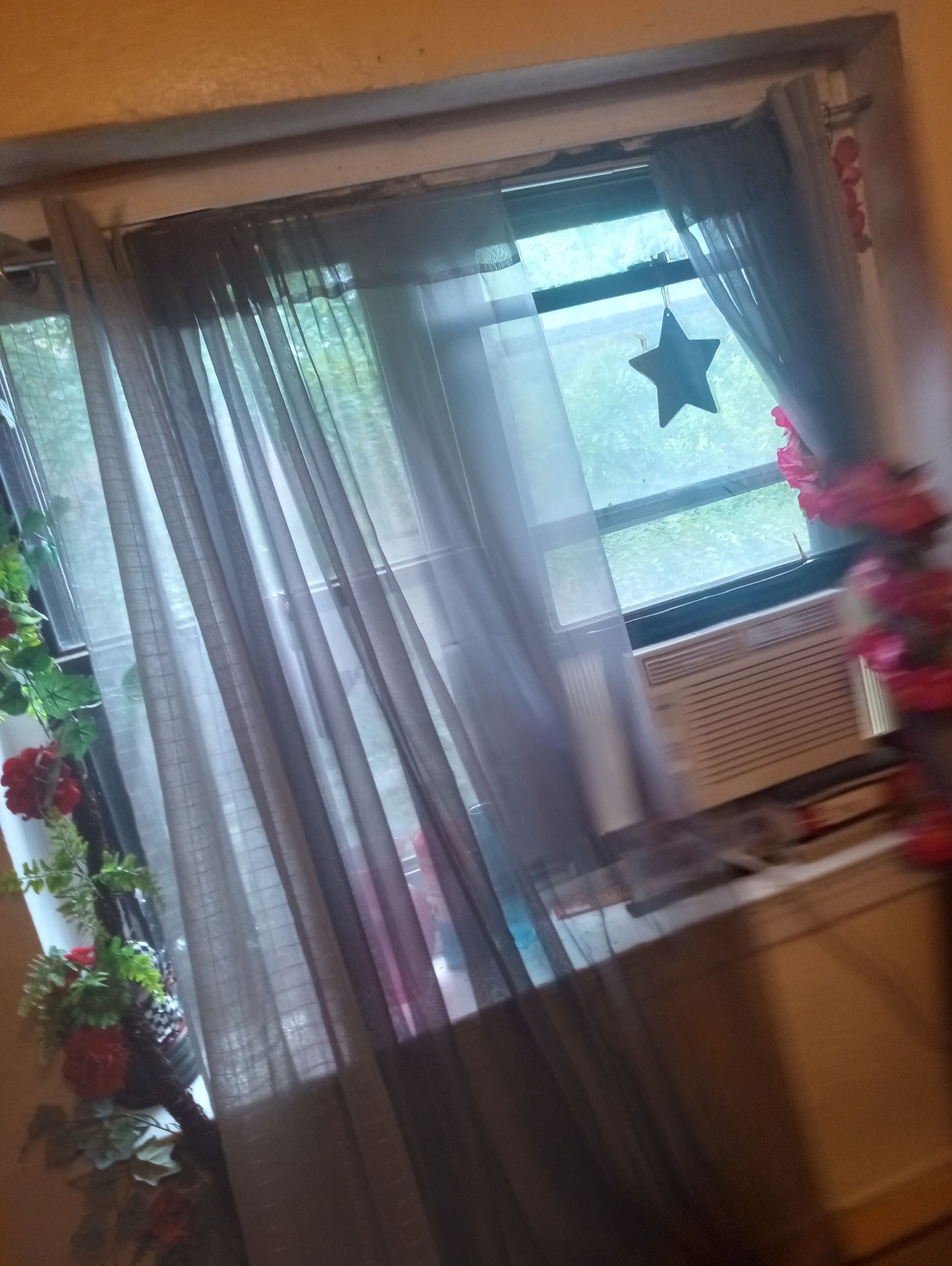 A window with sheer curtains, a star decoration, and a floral arrangement.