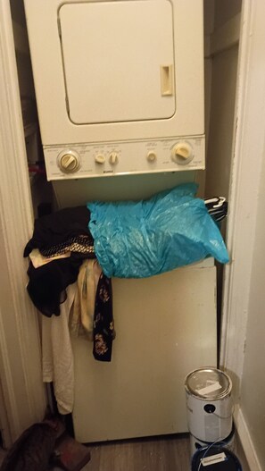 Un lavadero con lavadora, tendedero y cubo de basura.