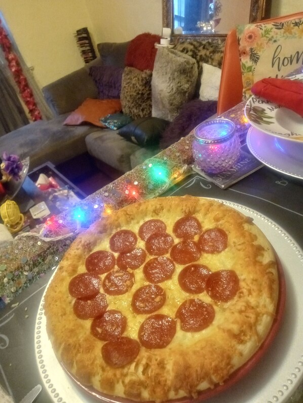 A pizza with pepperoni slices on a plate, a glass table, and a living room in the background with a couch and decorative pillows.