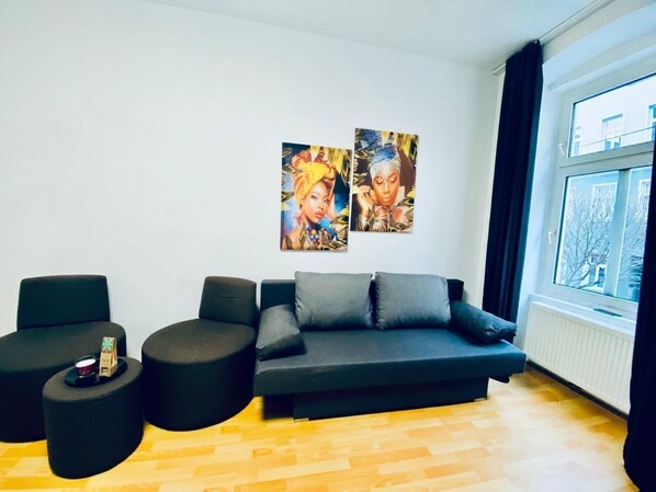 Un salon moderne avec un canapé de couleur foncée, deux fauteuils noirs et une table basse. Deux œuvres d’art encadrées ornent le mur.