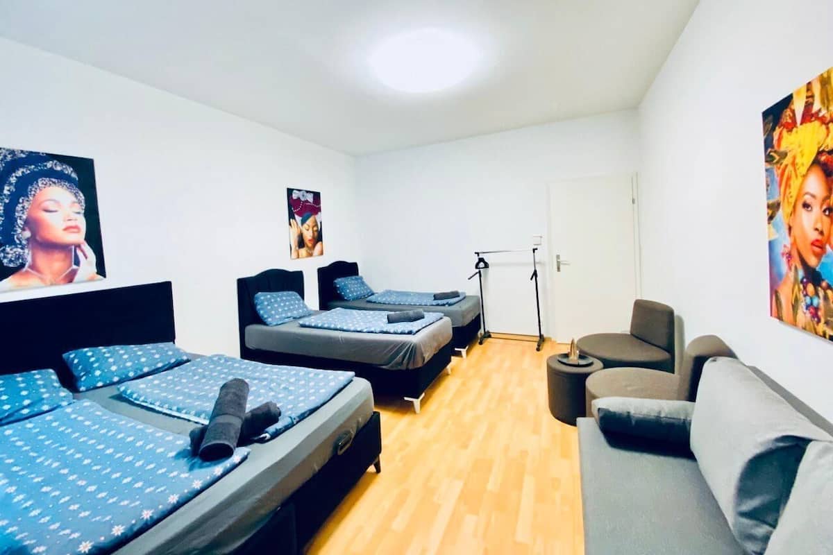 Quarto com três camas, um sofá cinza e um abajur.