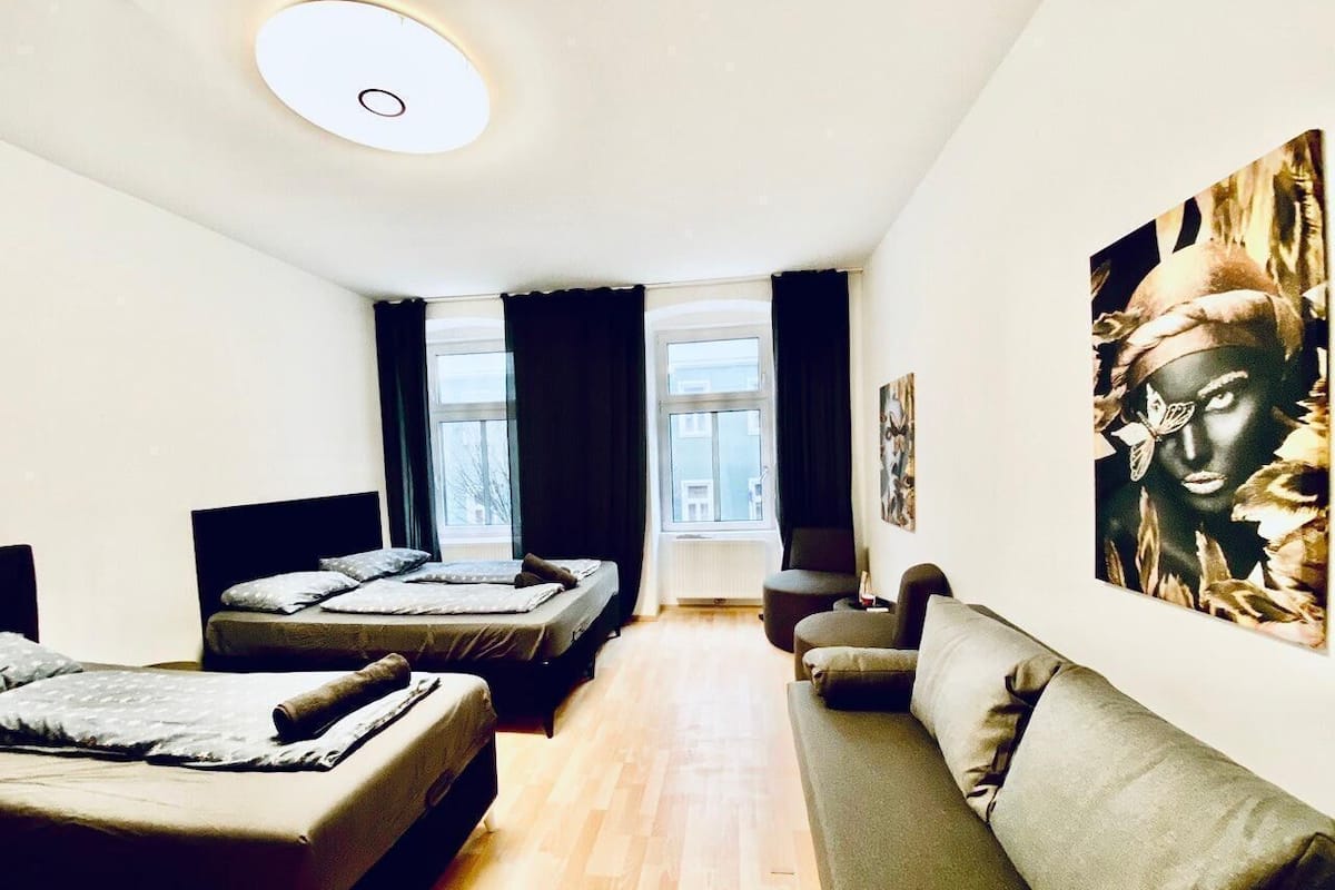 Quarto de hotel moderno com duas camas de solteiro, um sofá, uma janela grande e uma obra de arte na parede.