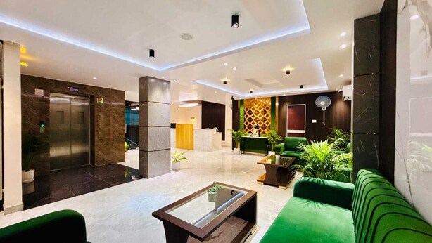 Um lobby moderno com balcão de recepção, assentos verdes e um elevador.