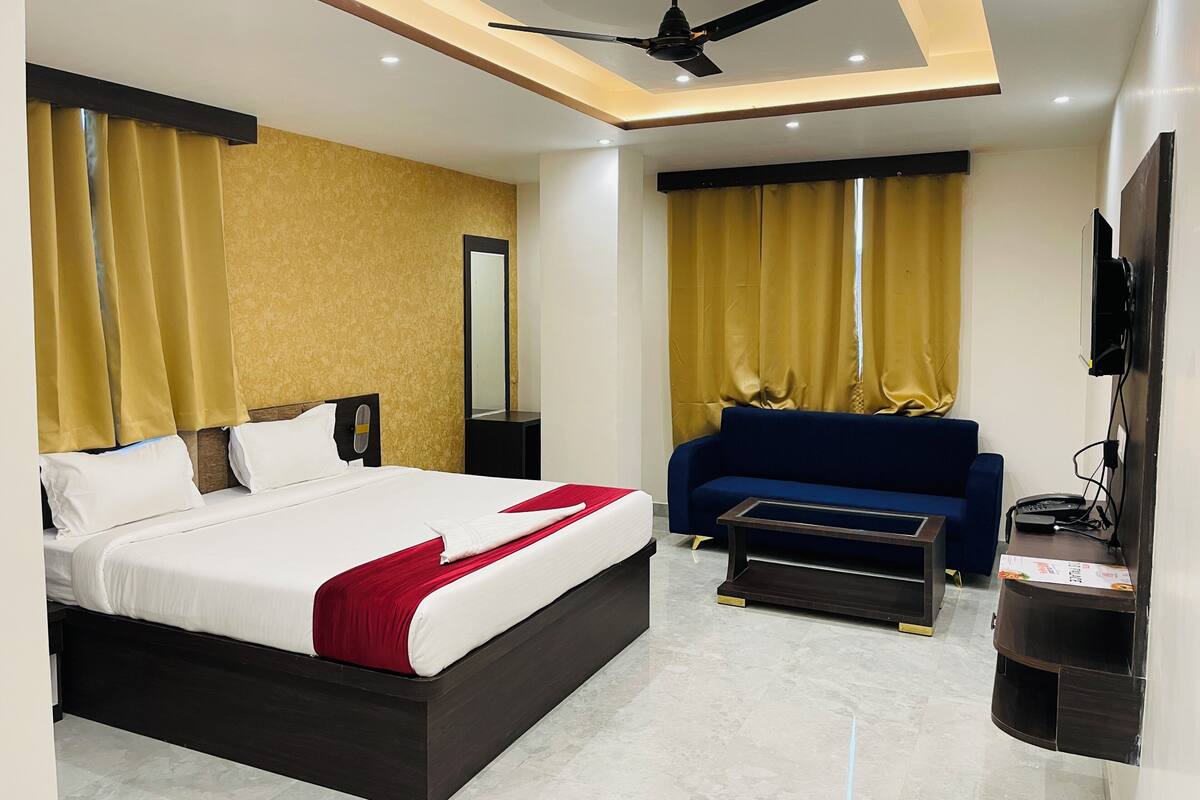 A modern hotel room with a large bed, a sofa, a TV, and a ceiling fan.