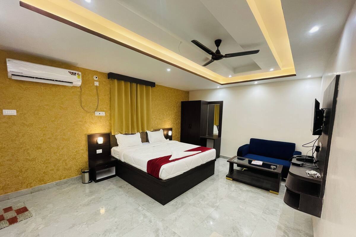 A modern hotel room with a large bed, a sofa, a TV, and a ceiling fan.