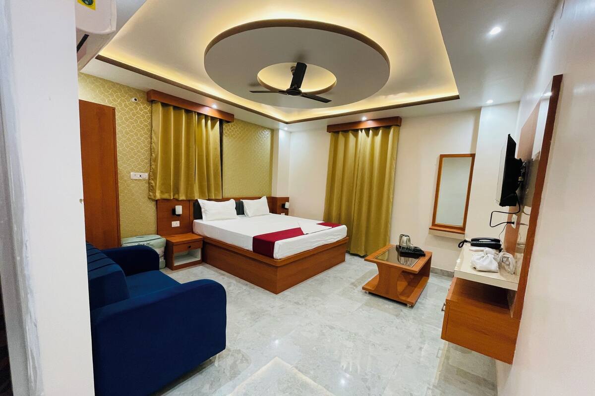 A hotel room with a bed, a sofa, a small table, a mirror, and a ceiling fan.