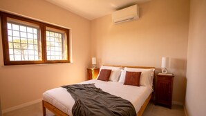 A bedroom with a bed, two bedside tables, a window, and an air conditioning unit.