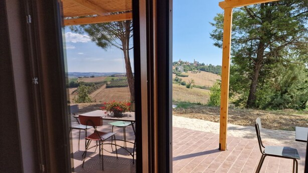 A patio with a table and chairs, a view of rolling hills, and a wooden pergola.