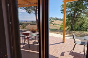 A patio with a table and chairs, a view of rolling hills, and a wooden pergola.
