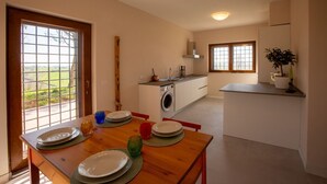 A modern kitchen with a washing machine, dining area with plates and glasses, and a view through a window.
