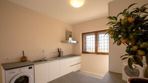 A compact kitchen with a washing machine, a sink, and a window with blinds.