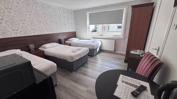 Habitación de hotel con dos camas, una mesita con un control remoto y un ventanal con vistas al exterior.
