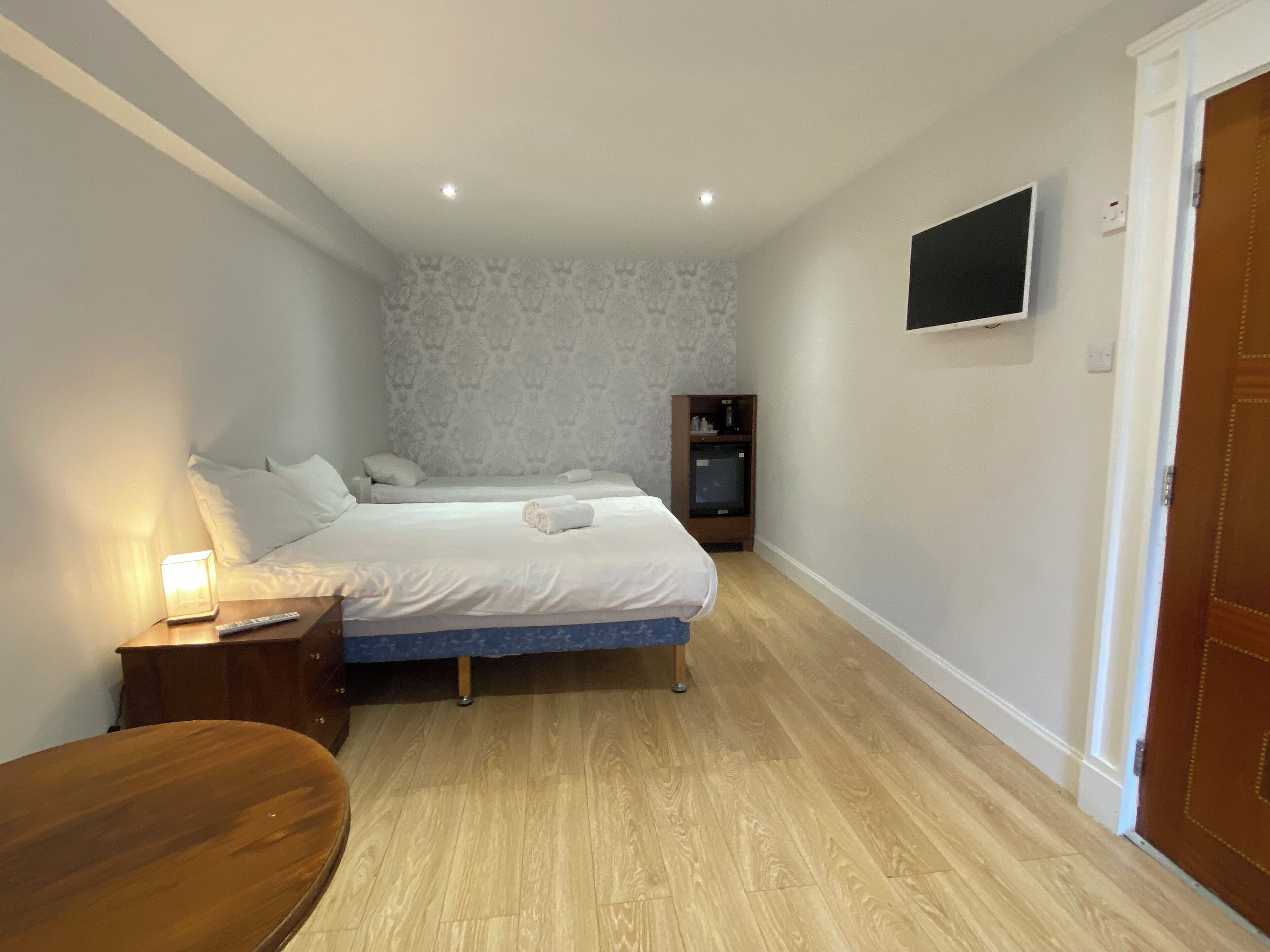 Un dormitorio con dos camas, un televisor montado en la pared, un armario de madera y una silla de madera.