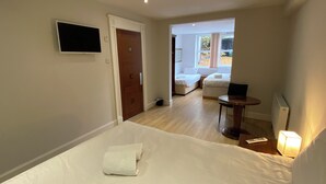 A hotel room with a bed, a desk, a chair, a TV, and a window with a view of the outside.