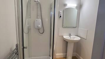 Une salle de bain moderne avec une douche à parois de verre, un lavabo sur colonne et un miroir au-dessus du lavabo.
