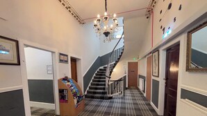 A hallway with a checkered carpet, a staircase, a chandelier, and a display of books.