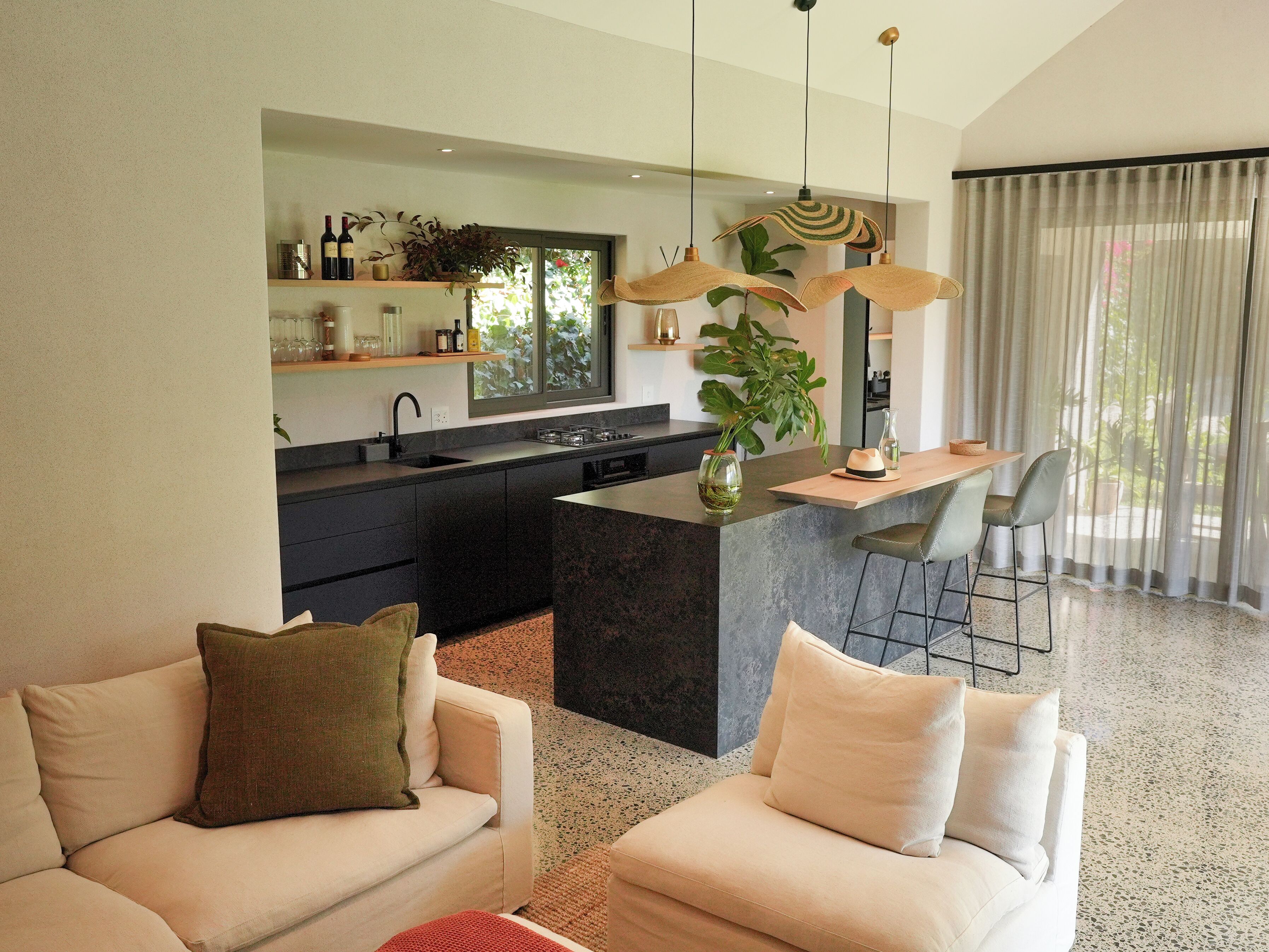 Cozinha moderna com ilha central, banquetas de bar e área de jantar com uma janela grande.