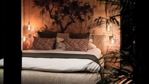 A bedroom with a large bed, zebra-patterned pillows, a tree mural on the wall, and hanging light bulbs. - Private Villa with pool in Cape Town (Cape Town)