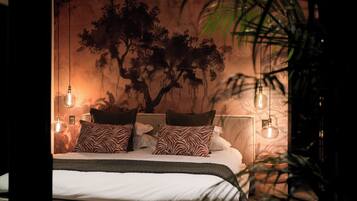 A bedroom with a large bed, zebra-patterned pillows, a tree mural on the wall, and hanging light bulbs.