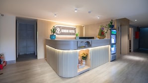 A hotel reception area with a modern design, featuring a reception desk, a digital screen, and a plant display. - Bin Bin Hotel 15 - Near Feliz En Vista (Ho Chi Minh City)