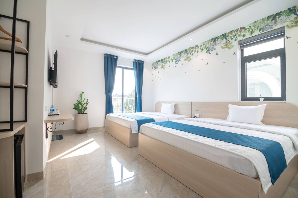 A hotel room with two beds, a TV mounted on the wall, a potted plant, and a window with curtains.