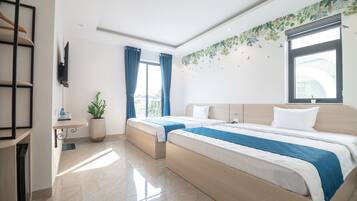 Habitación de hotel con dos camas, un televisor montado en la pared, una planta en maceta y una ventana con cortinas.