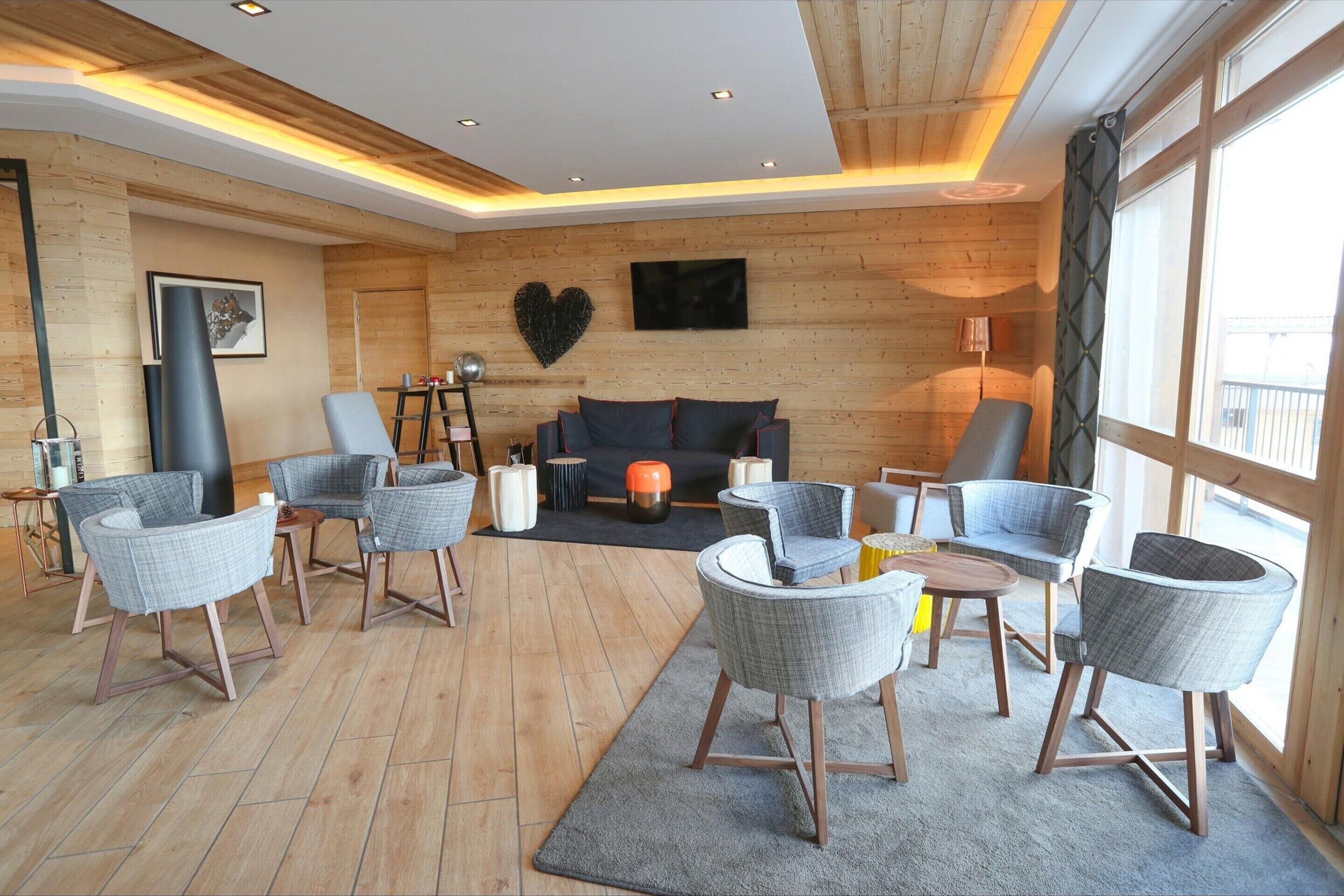 A modern living room with wooden walls, a grey sofa, and multiple grey armchairs.