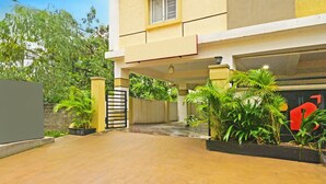 Un edificio residencial con entrada protegida por un portón, plantas en macetas y una puerta visible con el número rojo.