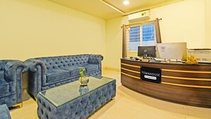 Un área de recepción con un sofá azul, una mesa de centro de vidrio, un mostrador de recepción y un ventilador de techo.