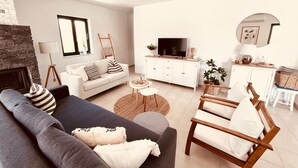 En moderne stue med sofa, lænestol, fjernsyn og pejs.