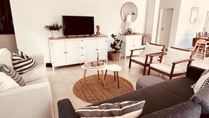 En moderne stue med sofa, lænestole, sofabord og et fjernsyn på et hvidt skab.