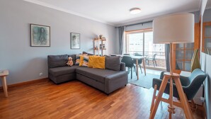 Ein modernes Wohnzimmer mit einem grauen Ecksofa, Holzboden und einem Essbereich mit Tisch und Stühlen.