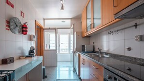 Eine moderne Küche mit Mikrowelle, Herd und Spüle. An der Wand hängt eine Uhr und ein Feuerlöscher ist vorhanden.