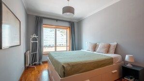 Ein Schlafzimmer mit einem Bett, einem Nachttisch, einem Heizkörper, einem Fenster mit Vorhängen und einer Kleiderstange.