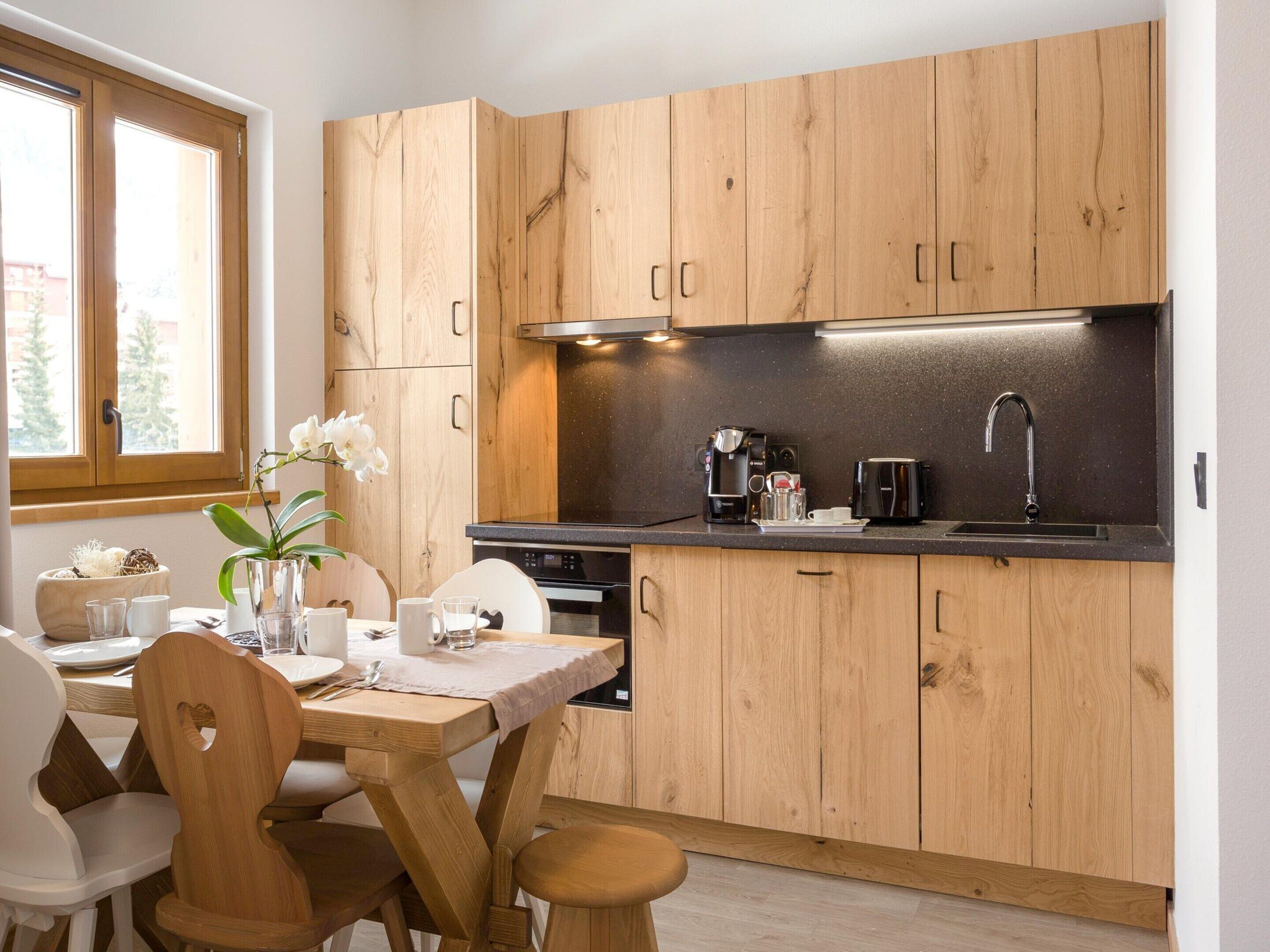 A modern kitchen with wooden cabinets, a black countertop, and a window with a view of trees.