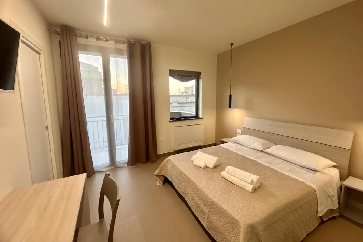 A hotel room with a bed, a desk, a chair, a window with curtains, and a view of the outside.