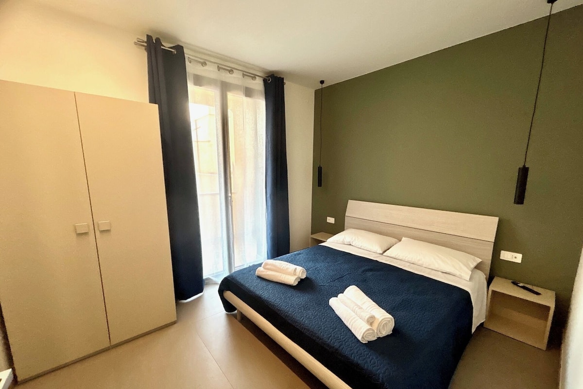 A bedroom with a bed, a nightstand, a wardrobe, and a window with curtains.