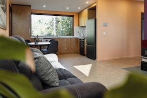 A modern kitchen with a large window, a dining table, and a sofa in the foreground. - Hidden Retreat - Off Grid (West Launceston)